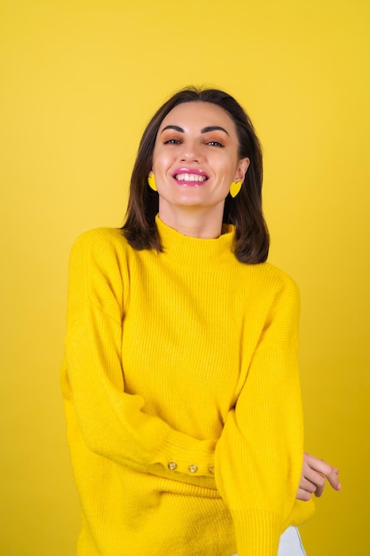 Mujer joven con un acogedor suéter amarillo con brillo rosa brillante sonríe dulcemente, de buen humor, irradia una actitud positiva