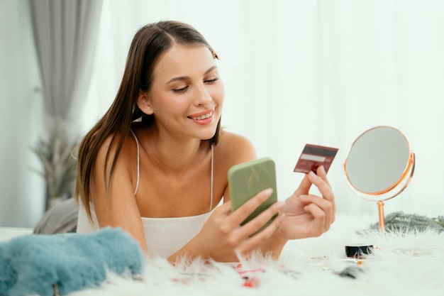 Mujer joven acostada en la cama usando una aplicación de pago en línea Desvelando