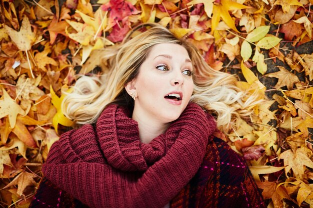 Foto mujer joven acostada en las hojas de otoño