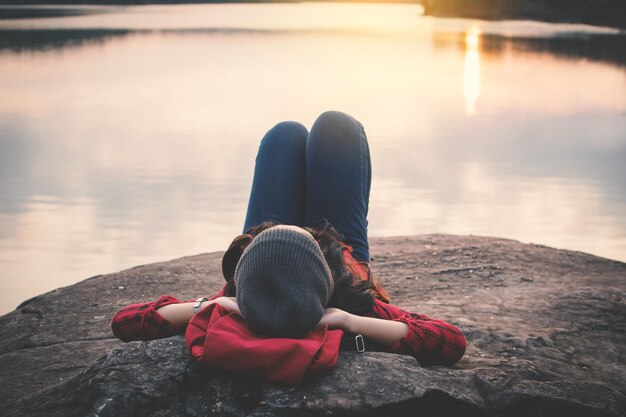 Mujer joven acostada en una roca junto al lago contra un cielo despejado