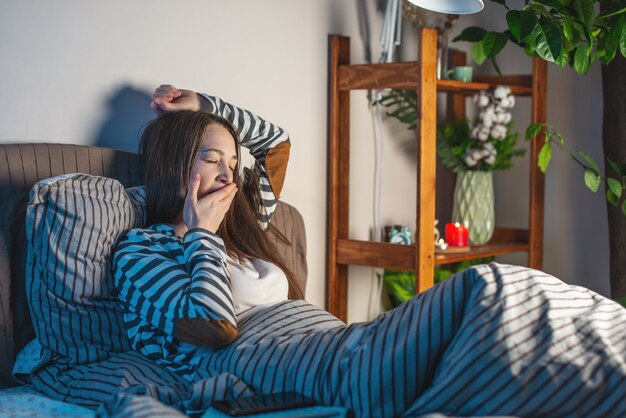 Mujer joven, acostado, en, ella, acogedor, cama, estirar, y, bostezar