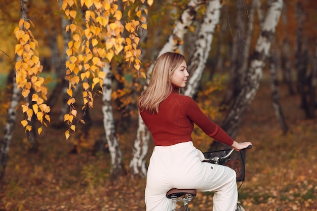 Mujer joven activa feliz montando bicicleta en el parque otoño