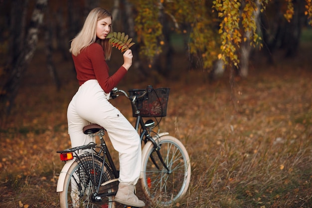 Mujer joven activa feliz montando bicicleta en el parque otoño