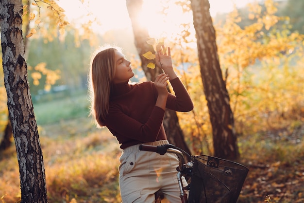 Mujer joven activa feliz montando bicicleta vintage en el parque de otoño al atardecer.