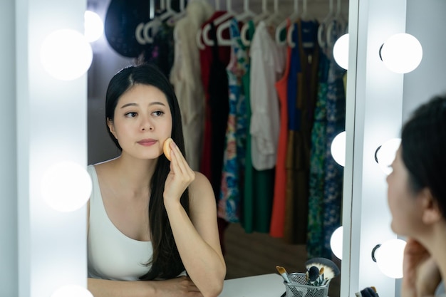 Mujer joven actriz coreana aplicando rubor en su cara con un espejo de polvo con bombillas en el vestidor. concepto de cuidado de la piel. animador asiático en backstage preparándose para el maquillaje de rendimiento
