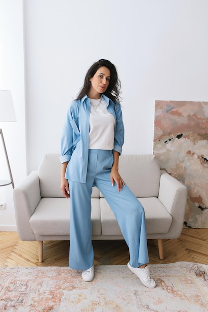 Mujer joven adulta está descansando en un hermoso vestido azul femenino en una habitación luminosa junto a la ventana relajarse