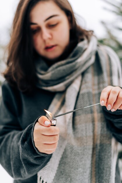 Mujer joven adulta con luces de Bengala en el fondo del bosque de pinos de invierno