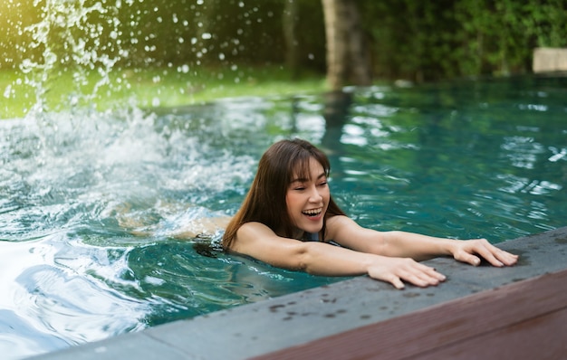 Mujer joven aferrarse al borde de la piscina y salpicaduras de agua con los pies