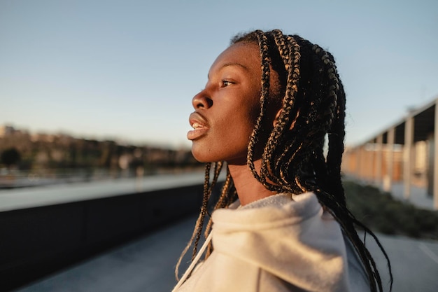 Mujer joven africana con rastas de perfil contemplando la ciudad