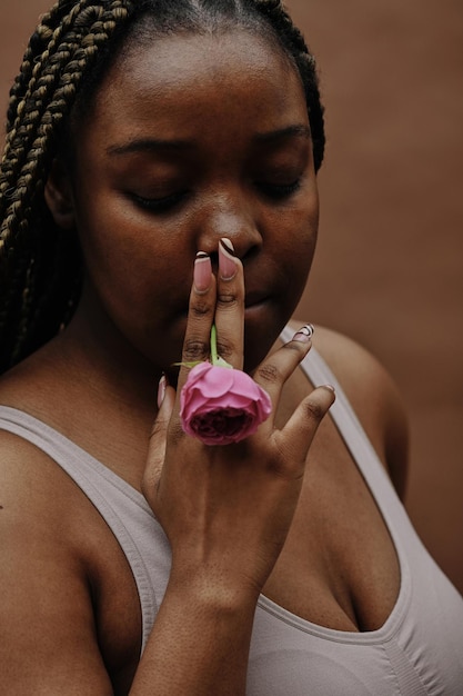 Mujer joven africana con trenzas sosteniendo rosa rosa en la boca y fumándola como cigarrillo