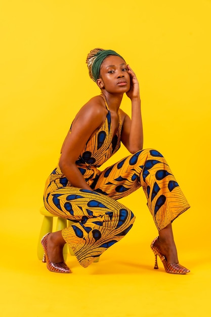 Foto mujer joven africana en vestido tradicional sobre fondo amarillo mirada seductora