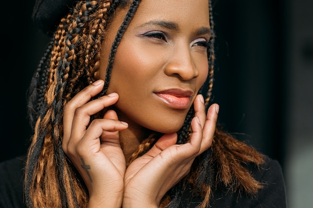 Mujer joven afroamericana complacida. Seductora mujer bonita sobre fondo oscuro, elegante corte de pelo, concepto de felicidad