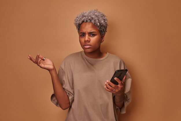 Mujer joven afroamericana enojada que sostiene el teléfono celular irritada por un dispositivo roto