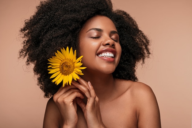 Mujer joven afroamericana con piel perfecta sosteniendo un girasol