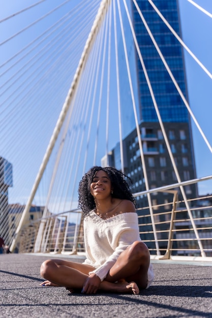 Mujer joven afroamericana en el retrato de la ciudad de una mujer joven sentada en un puente