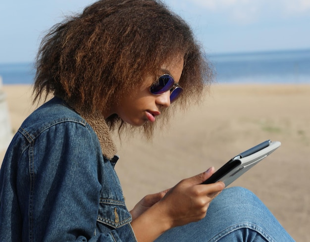 Mujer joven afroamericana con tableta en la playa