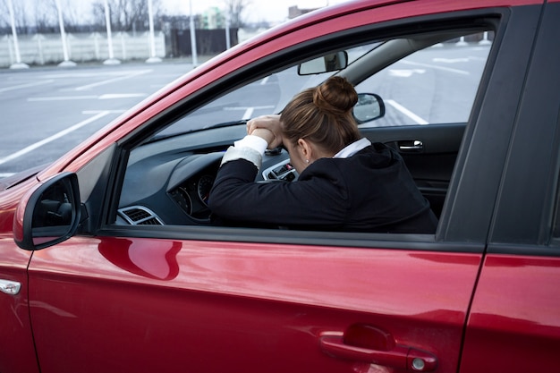 Mujer joven agotada durmiendo mientras conduce un coche