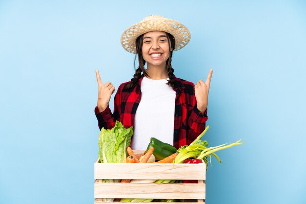 Mujer joven agricultor sosteniendo verduras frescas en una canasta de madera apuntando hacia una gran idea
