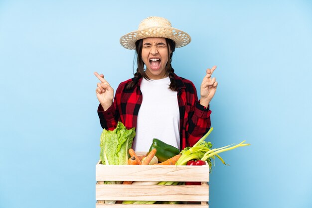 Mujer joven agricultor sosteniendo verduras frescas en una canasta de madera con los dedos cruzando