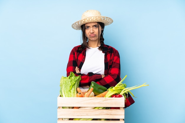 Mujer joven agricultor sosteniendo verduras frescas en una canasta de madera sintiéndose molesto