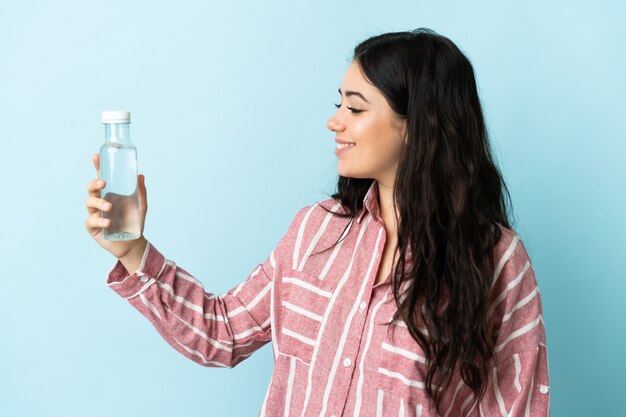 Mujer joven con un agua aislada en la pared azul con expresión feliz