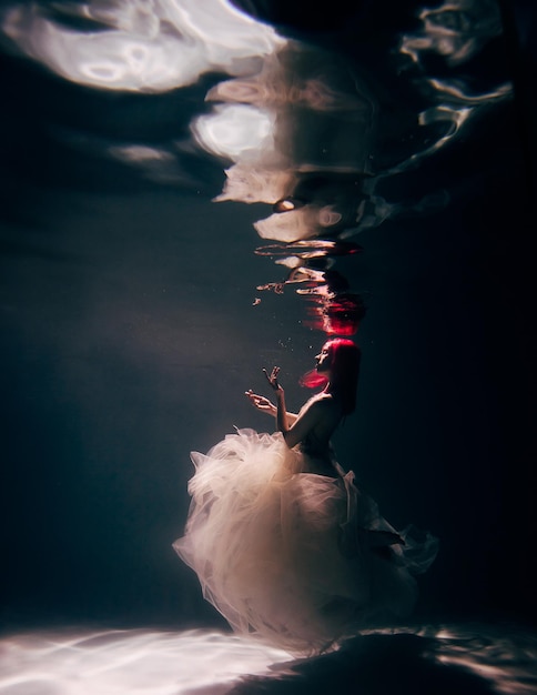 Mujer joven bajo el agua en un hermoso vestido de tiro bajo el agua