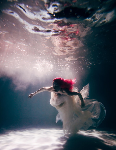 Mujer joven bajo el agua en un hermoso vestido de tiro bajo el agua