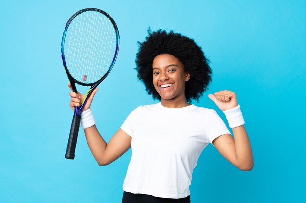 Mujer joven aislada en azul jugando tenis y orgulloso de sí mismo