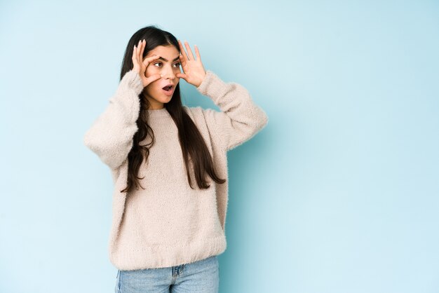 Mujer joven aislada en azul mirando sorprendido