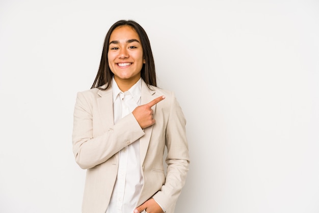 Mujer joven aislada en un blanco sonriendo y apuntando a un lado, mostrando algo en el espacio en blanco.