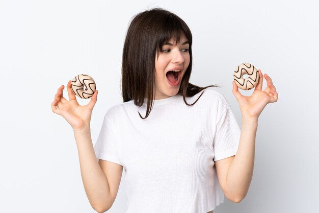 Mujer joven aislada en blanco sosteniendo donas y sorprendido