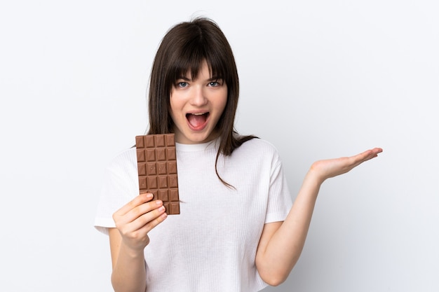 Mujer joven aislada en blanco tomando una tableta de chocolate y sorprendido