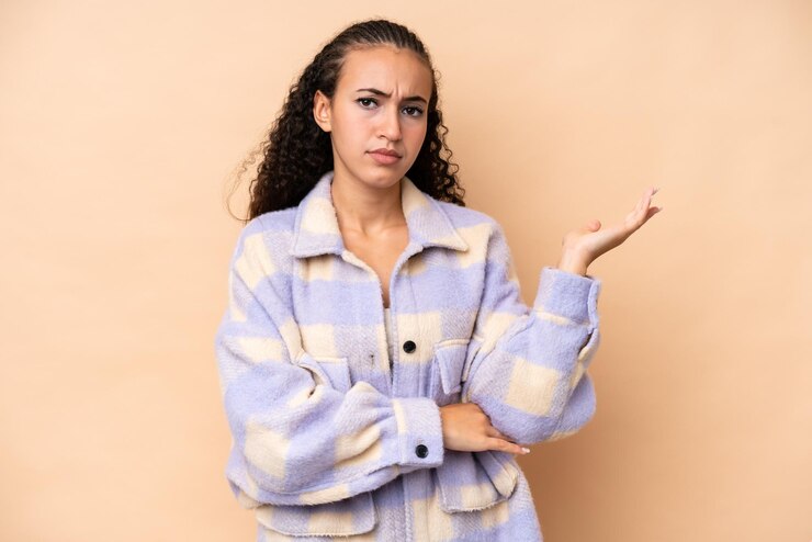 Foto mujer joven aislada en fondo beige con dudas