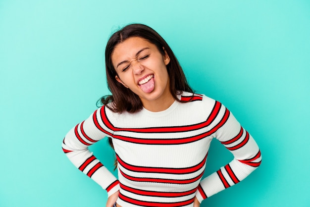 Mujer joven aislada en la pared azul divertido y amigable sacando la lengua