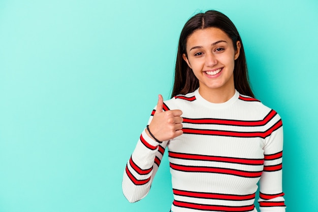 Mujer joven aislada en la pared azul sonriendo y levantando el pulgar hacia arriba