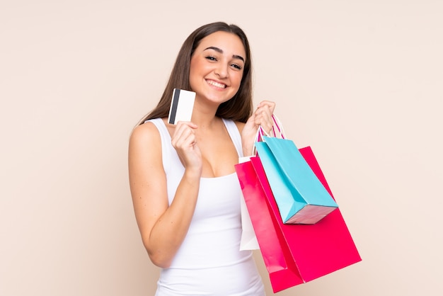 Mujer joven aislada en la pared de color beige con bolsas de compra y una tarjeta de crédito