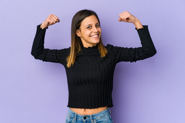 Mujer joven aislada en la pared púrpura mostrando gesto de fuerza con los brazos, símbolo del poder femenino