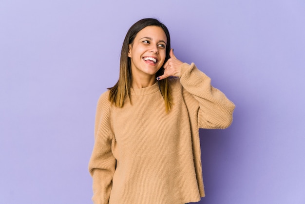 Mujer joven aislada en la pared púrpura que muestra un gesto de llamada de teléfono móvil con los dedos