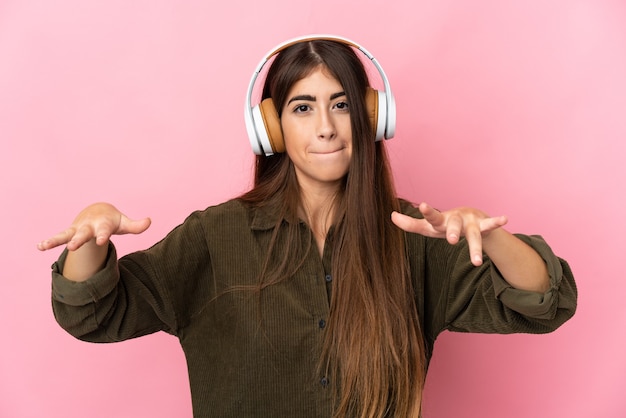 Mujer joven aislada en la pared rosa escuchando música y bailando