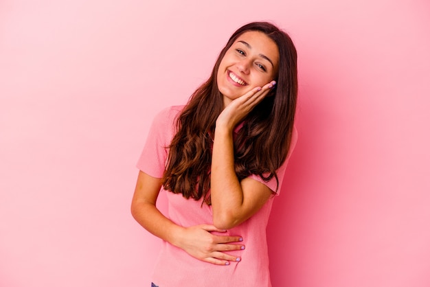 Mujer joven aislada en la pared rosa se ríe felizmente y se divierte manteniendo las manos en el estómago