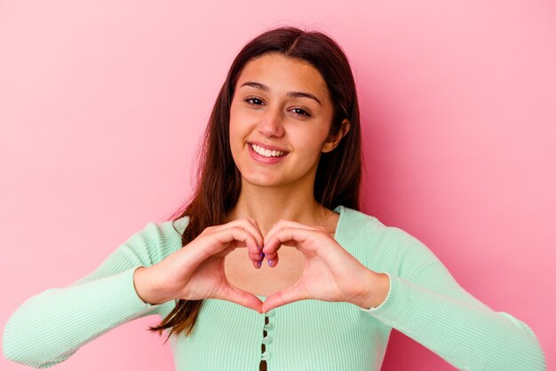 Foto mujer joven aislada en la pared rosa sonriendo y mostrando una forma de corazón con las manos