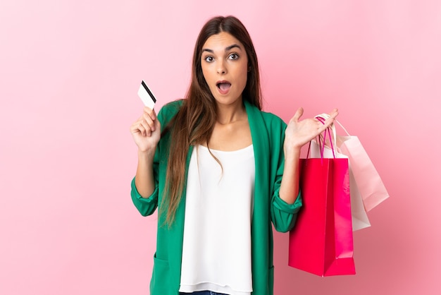 Mujer joven aislada en la pared rosa sosteniendo bolsas de compras y sorprendido