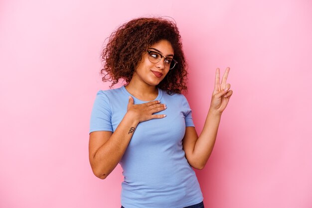 Mujer joven aislada en la pared rosa tomando un juramento, poniendo la mano en el pecho