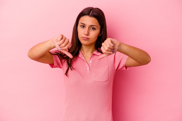 Mujer joven aislada en la pared rosada mostrando un gesto de disgusto, pulgares hacia abajo