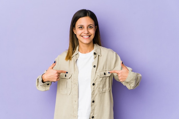 Foto mujer joven aislada en persona púrpura apuntando con la mano a un espacio de copia de camisa, orgulloso y seguro