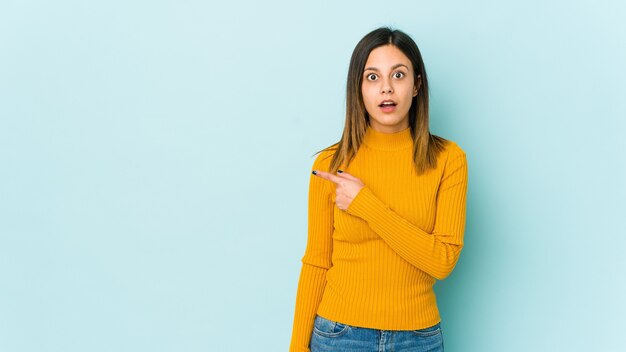 Mujer joven aislada sobre fondo azul apuntando hacia el lado