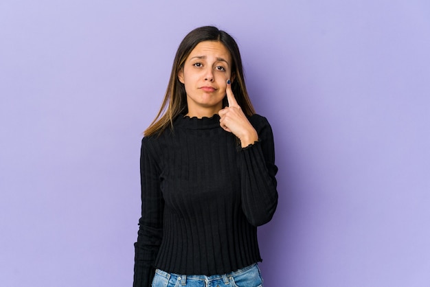 Mujer joven aislada sobre fondo púrpura llorando, infeliz con algo, concepto de agonía y confusión.