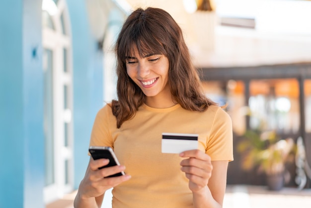 Mujer joven al aire libre comprando con el móvil con tarjeta de crédito