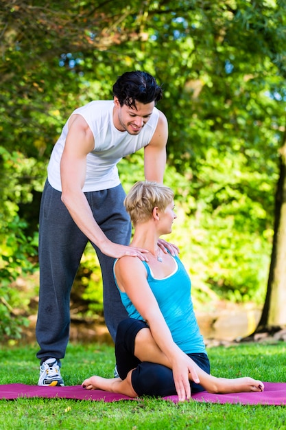 Mujer joven al aire libre haciendo yoga con entrenador