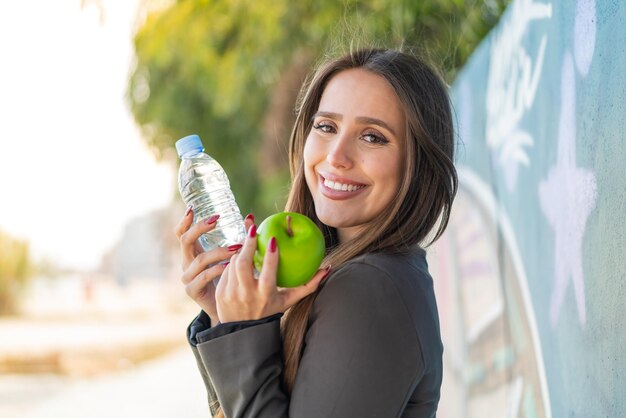 Foto mujer joven al aire libre con una manzana y con una botella de agua.